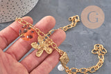 Collier DIY en chaîne dorée acier inoxydable 304 avec breloques fleur, perle nacrée et médaillon sur fond gris.