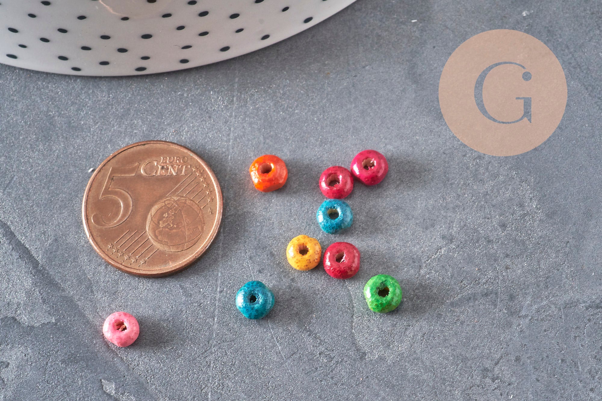 Perles rondelles en bois multicolores de 5x3mm disposées à côté d'une pièce de 5 centimes pour l'échelle.