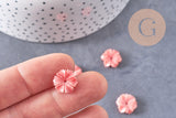 Close-up of fingertips holding a pink, flower-shaped resin bead, 13mm, with similar beads scattered below; product: EP-Perle fleur résine rose, x5, for jewelry making.