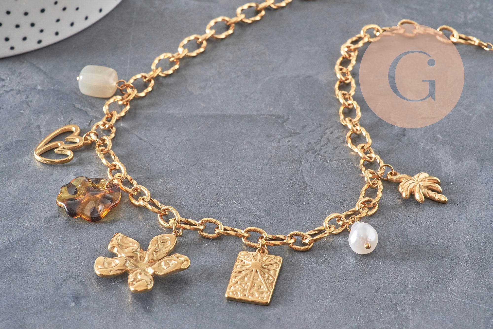 Collier DIY en chaîne dorée acier inoxydable 304 avec breloques cœur, fleur, perles nacrées et médaillons sur fond gris.